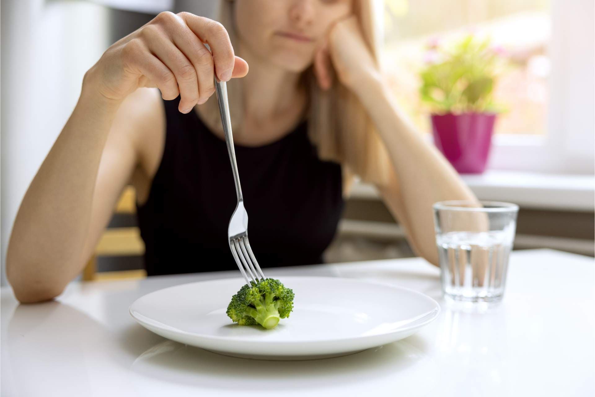 Person sitting at a table looking at a small portion of food, representing struggles with eating disorders and the need for emotional and nutritional support.